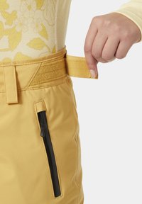 Geel sneeuwbroek met een gladde textuur, voorzien van een zwarte ritszak, verstelbare haak-en-lus tailleband en zijdetails.