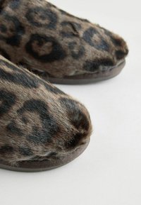 Papuci cu imprimeu de leopard, confecționați din blană moale și texturată, cu vârful rotunjit și o talpă maro durabilă, având pete negre pe un fundal bej.