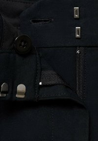 Black fabric with a button closure, metal hardware, and a zipper. Features a textured interior with visible stitching and fastening details.