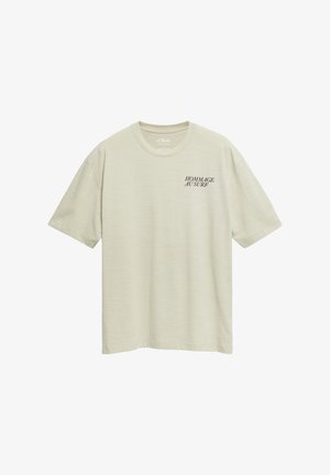 Jasnobeżowy T-shirt z krótkim rękawem i okrągłym dekoltem, z czarnym nadrukiem "HOMMAGE AU SURF" na górnej lewej części klatki piersiowej.