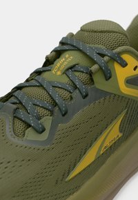 Oliivroheline Altra Torin 8 jalatsid Gore-Tex materjalist, tekstuurse meshiga, hallide paeltega ja kollase brändi logo detailiga.