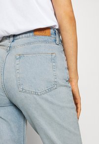 Svetle modré džíny s uvolněným střihem, vybavené koženou nášivkou označenou 'BDG' na pásku a standardními zadními kapsami.