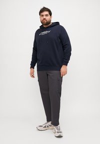Navy sweatshirt with drawstrings and logo, paired with gray cargo pants featuring side pockets and light-colored sneakers.