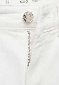 Gros plan sur un tissu en denim blanc avec un bouton argenté et une fermeture éclair métallique partiellement ouverte.