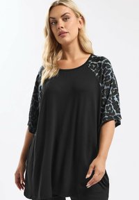 Schwarze Tunika mit Ärmeln im Leopardenprint. Weicher Stoff, lockere Passform, runder Ausschnitt und schulterfreies Design. Kurze Ärmel, lässiger Stil.