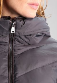 Gray puffer jacket featuring horizontal quilted pattern, high collar, and metallic zipper. Soft, shiny exterior with contrasting dark zipper trim.