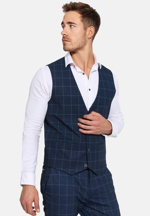 Marineblauw geruite vest met een slim fit, voorzien van een V-hals ontwerp, twee voorzakken en een bijpassende pantalon, gedragen over een wit overhemd.