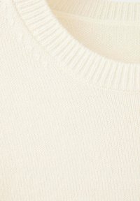 Gros plan d’un pull tricoté couleur crème montrant l’encolure ronde côtelée et le tissu doux texturé.