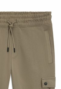 Baumwoll-Jogginghosen in hellkhaki mit einem elastischen Bund, Kordelzug, Seitentaschen und einer geknöpften Cargotasche am Bein.