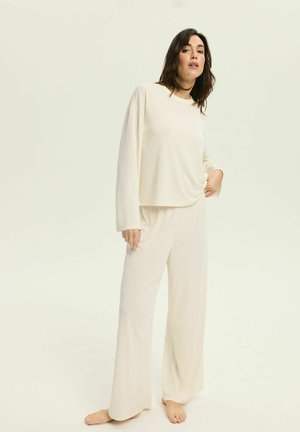 Beige Loungewear-Set bestehend aus einem locker sitzenden Langarmshirt und weit geschnittenen Hosen aus weichem Stoff. Einfaches, minimalistisches Design.