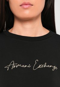Zwarte sweatshirt met een ronde hals en een gouden geborduurd "Armani Exchange" logo op de borst. Zachte, gladde stoftextuur.