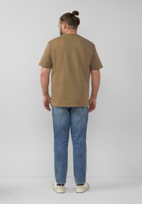 Olijfgroene katoenen t-shirt met korte mouwen, gecombineerd met lichtblauwe spijkerbroek en witte sneakers, gezien vanaf de achterkant.