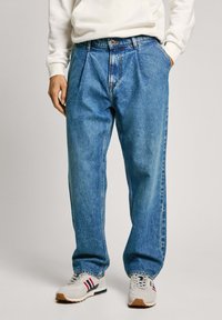 Ljust blå denimjeans med avslappnad passform, med veck, knäppning och synliga sömmar. Bärs med vita sneakers.