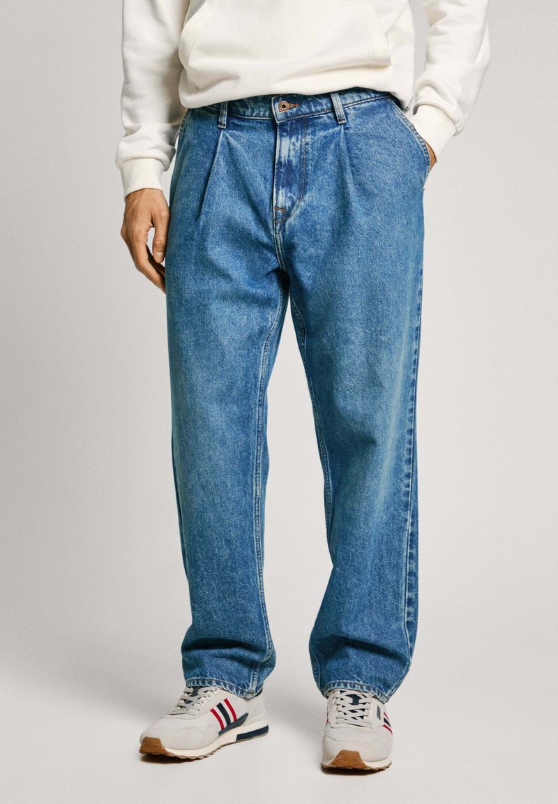 Ljust blå denimjeans med avslappnad passform, med veck, knäppning och synliga sömmar. Bärs med vita sneakers.