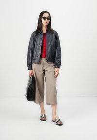 Giubbotto bomber in pelle nera, top aderente rosso, pantaloni beige a gamba larga, borsa nera e sandali con motivo a serpente. Gli occhiali da sole completano il look.