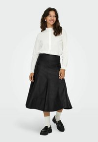 Svart läderkjol med en utsvängd design, parat med en vit skjorta med knäppning och svarta loafers. Utseendet fulländas med vita ankelsockor.