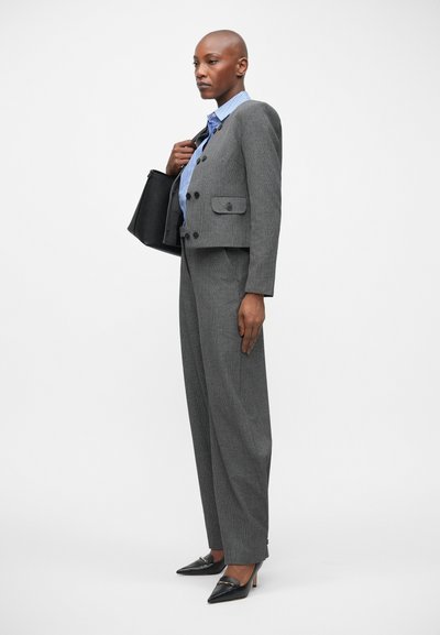 Grijs houndstooth pak met een cropped blazer, brede broekspijpen en een blauw gestreept overhemd. Een zwarte tote bag en scherpe zwarte hakken maken de look compleet.