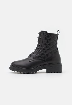 Botte de combat en cuir noir avec partie matelassée à la cheville, laçage avant, semelle épaisse et languette au talon.