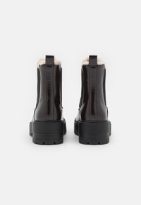 Black glossy ankle boots with textured sides, a plush lining visible at the top, and a thick, ridged sole for added grip.