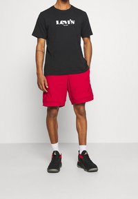 Černé bavlněné tričko s bílým logem "Levi's", doplněné červenými šortkami s kapsami a ohrnutým lemem, obuté s černými sportovními botami.