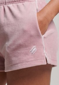 Los pantalones cortos de algodón rosa tienen una textura suave, bolsillos laterales, una cintura elástica y un logo bordado en blanco en el lado inferior izquierdo.