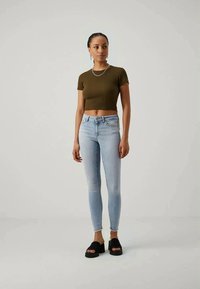Olivově zelené zkrácené tričko, světle modré skinny džíny a černé platformové sandály. Hladká textura, přiléhavý střih s vysokým pasem.