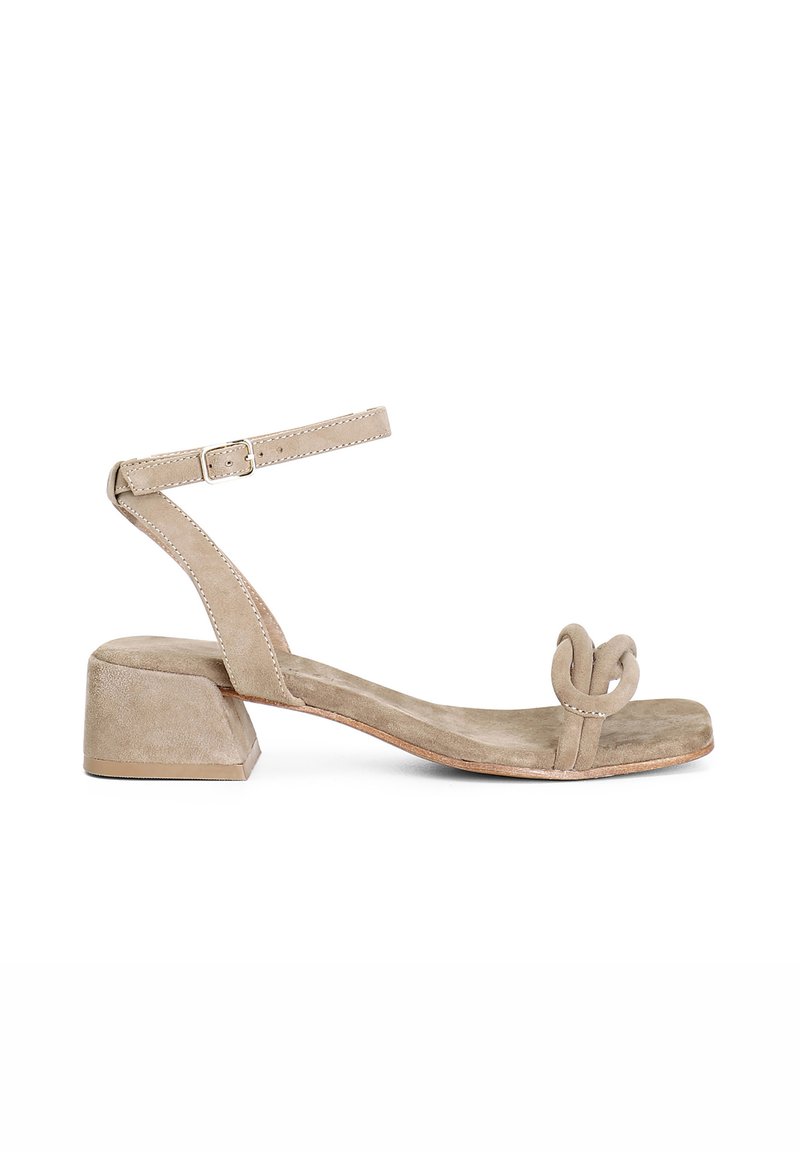 Beige svinskin ankelrem sandal med blockklack, med en böjd knuthållare vid tån, platt sula och en minimalistisk design.