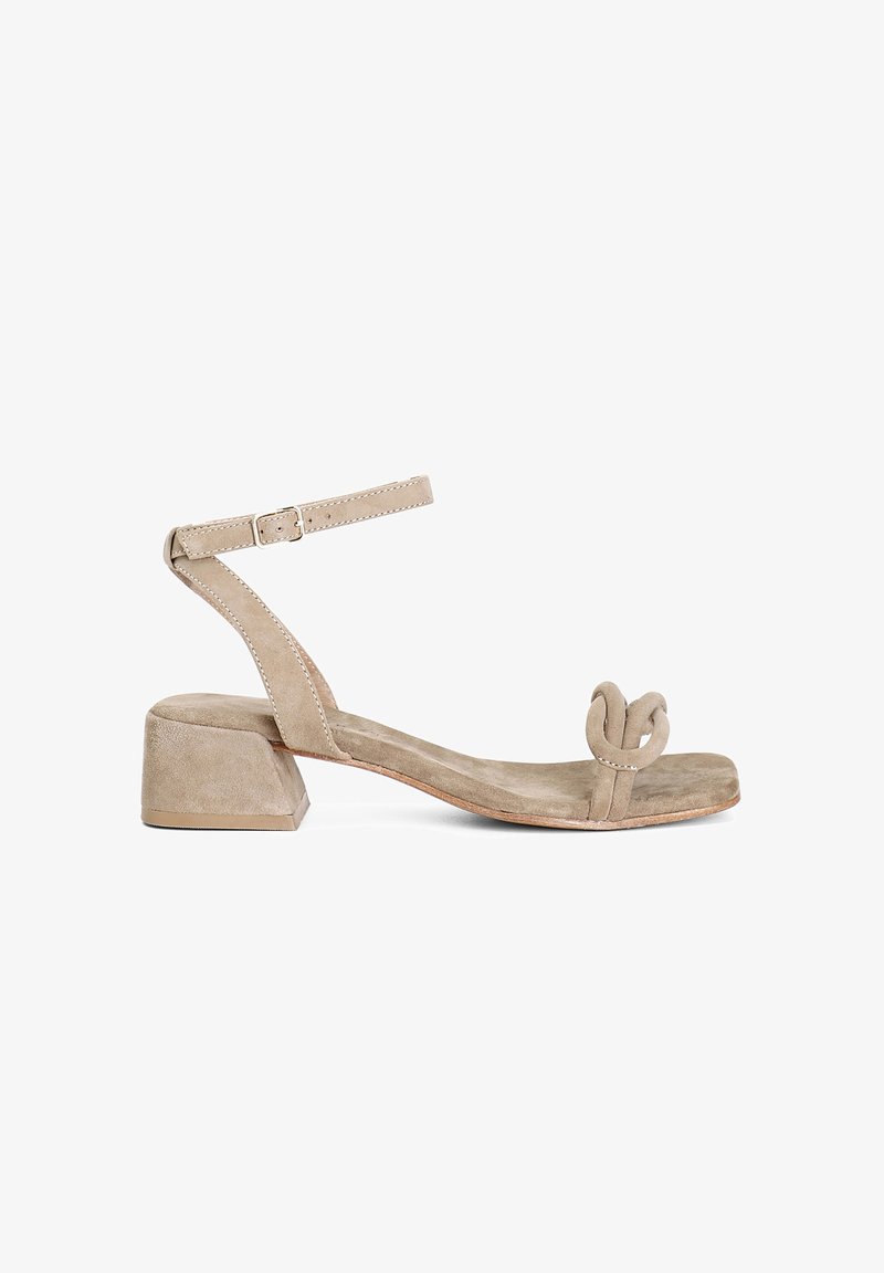 Beige mokkanahka ankle strap sandaali, jossa on lohkarekorko, kaareva solmupisto kärkiosassa, litteä pohja ja minimalistinen muotoilu.