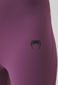 Lila sportos leggings sima, rugalmas anyagból. Fekete logóval a combon és fitted dizájnnal, lapos varrással.