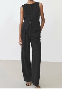 Černý lněný svetr s kulatým výstřihem a zapínáním na pět knoflíků, doplněný černými kalhotami s vysokým pasem, které mají volný střih a záhyby.