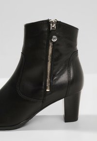 Bottine en cuir noir avec une fermeture éclair latérale et une surface texturée. Présente un talon épais et des détails cousus pour la structure.