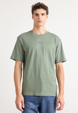 Olivengrøn bomulds t-shirt med rund halsudskæring, korte ærmer og prægede "BOSS" logo på brystet. Parret med blå denim jeans.