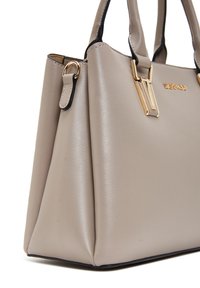 Sac à main en cuir synthétique beige avec quincaillerie dorée, forme structurée et double anses. Présente une texture lisse et un détail de logo.