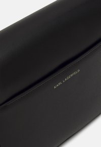Czarna skórzana kopertówka o gładkiej fakturze. Na przedzie znajduje się złote logo "KARL LAGERFELD" oraz elegancki design.