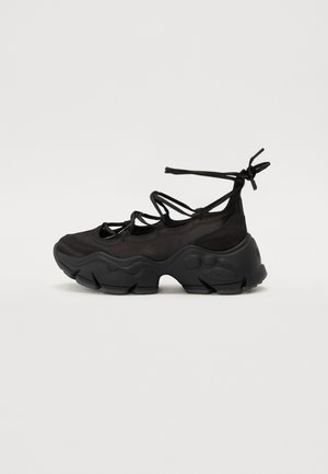 Baskets noires épaisses avec une semelle texturée épaisse et plusieurs fines sangles croisées sur le pied avec fermeture par lacets à la cheville.