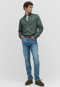 Groen overhemd met knopen, lichtblauwe jeans, een bruine riem en donkerbruin schoenen. Het overhemd heeft een gladde textuur met een kraag.