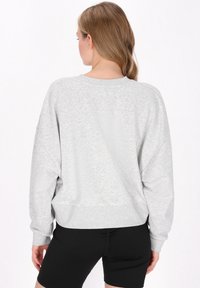 Světlé šedé, oversized mikiny s kleslými rameny a žebrovanými manžetami; měkká textura. Kombinováno s černými kraťasy, vytváří neformální vzhled.