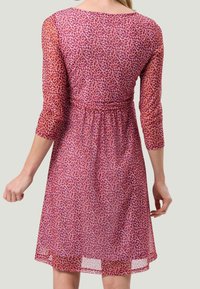 Robe transparente à manches longues avec un motif de feuilles violettes et roses, taille ajustée et jupe longueur genou avec un ourlet légèrement froncé.