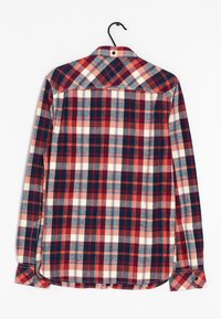 Camisa de franela a cuadros en rojo, azul marino y crema. Cuenta con un collar abotonado, mangas largas y un dobladillo curvado. Está hecha de una tela suave.