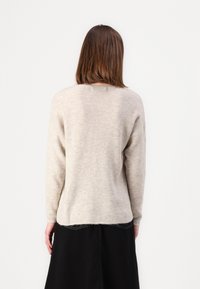 Maglione beige a maglia con una texture morbida, scollatura rotonda e spalle cadenti. Indossato su una gonna nera, con un design dal taglio rilassato.