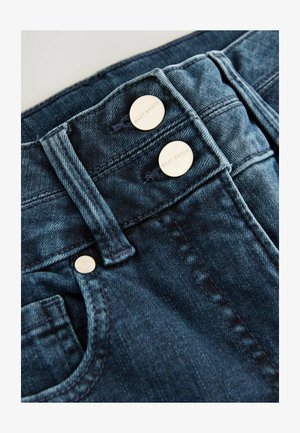 Denim jeans van donkerblauwe stof. Bevat twee zilveren knopen met "NEXT DENIM" gegraveerd, contrasterende stiksels en een gebogen zak.
