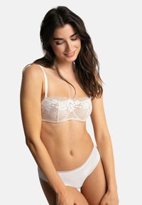 Soutien-gorge en dentelle blanche avec motif floral et panneaux transparents, complété par un slip blanc lisse avec une délicate bordure en dentelle le long des bords.