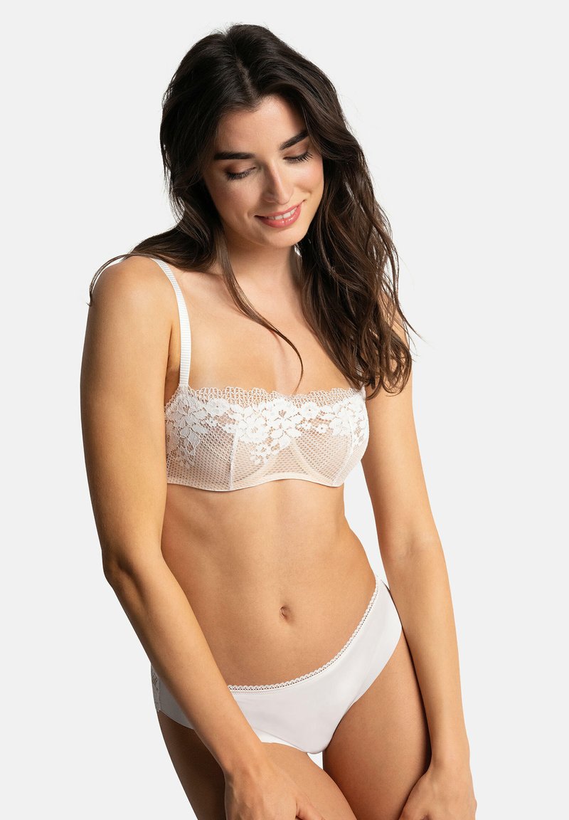 Soutien-gorge en dentelle blanche avec motif floral et panneaux transparents, complété par un slip blanc lisse avec une délicate bordure en dentelle le long des bords.