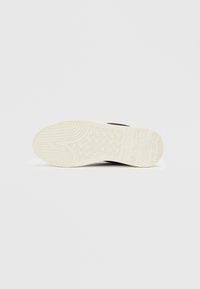 Brown sneaker with a textured rubber outsole, featuring a white midsole and patterned grooves for traction.