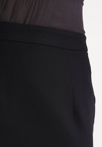 Černá krejčovská sukně s hladkou texturou, která má úzký pas a jemné detaily šití, navržená pro elegantní vzhled.