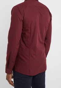 Bordeaux lange mouwen shirt met een puntkraag, slim fit en knoopmanchetten. Beschikt over een gladde textuur en een gebogen zoom aan de achterkant.