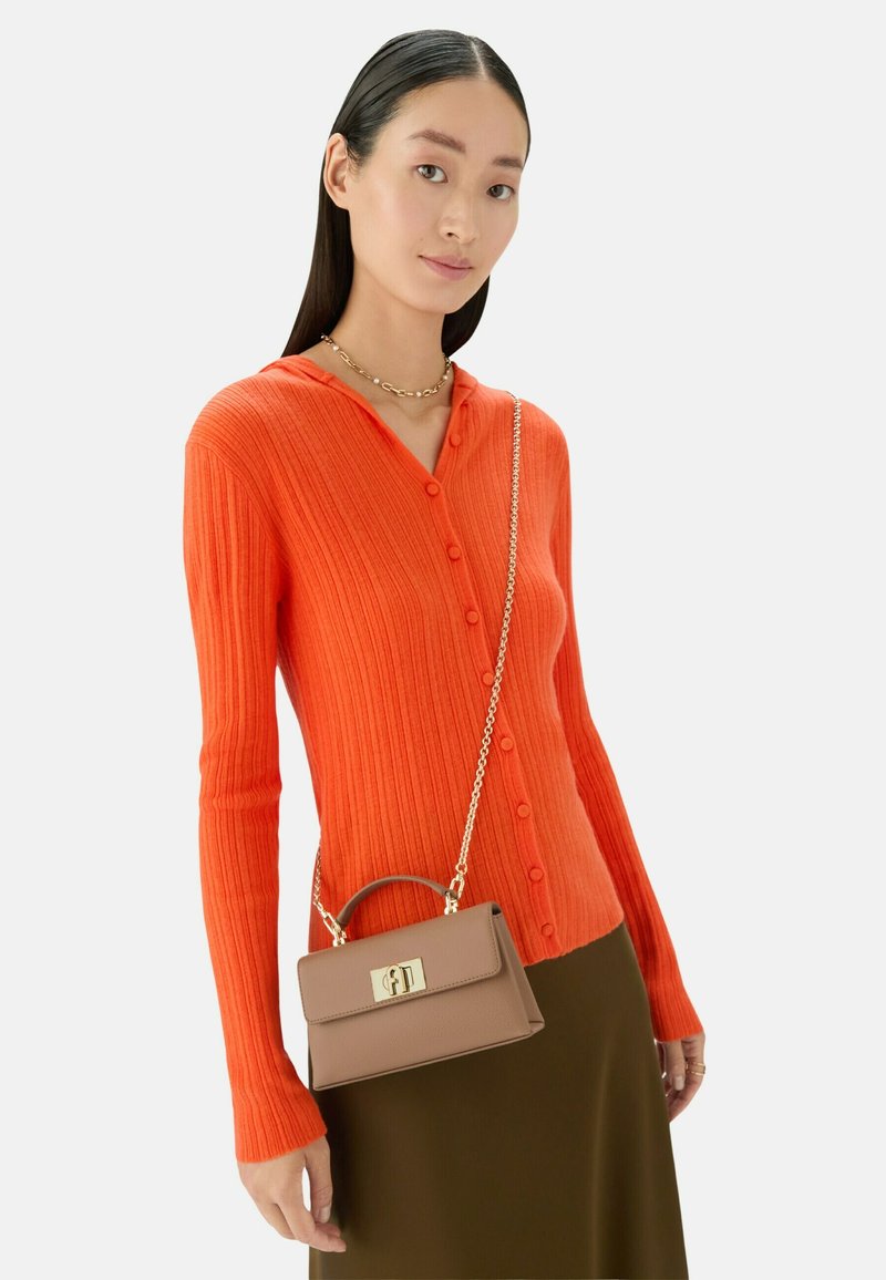Cardigan a coste di un brillante arancione con bottoni e cappuccio. Abbinato a una piccola borsa marrone con chiusura in oro e tracolla a catena.