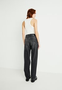Zwart hoge taille denim jeans met een ontspannen fit, voorzien van twee achterzakken en een knoopsluiting, gecombineerd met een wit tanktop.