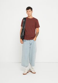 Bordeaux gestreepte t-shirt, relaxte pasvorm, gecombineerd met lichtblauwe wijde jeans. Zwarte schoudertas, witte sokken en beige sneakers met zwarte accenten.