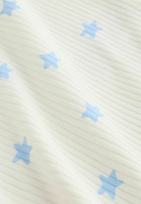 Bijela tkanina rebraste strukture s razbacanim svijetloplavim tiskanim zvjezdicama, prikazujući teksturu i mekane nabore.